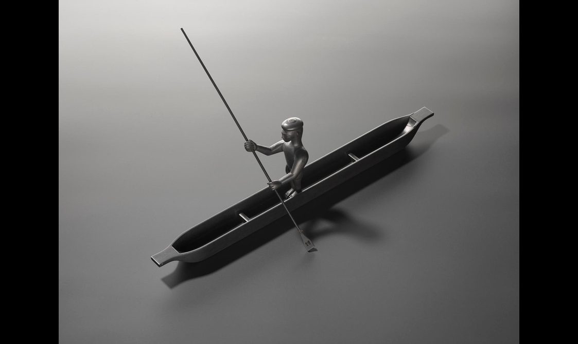A metal model of a person sitting in a canoe with a spear.