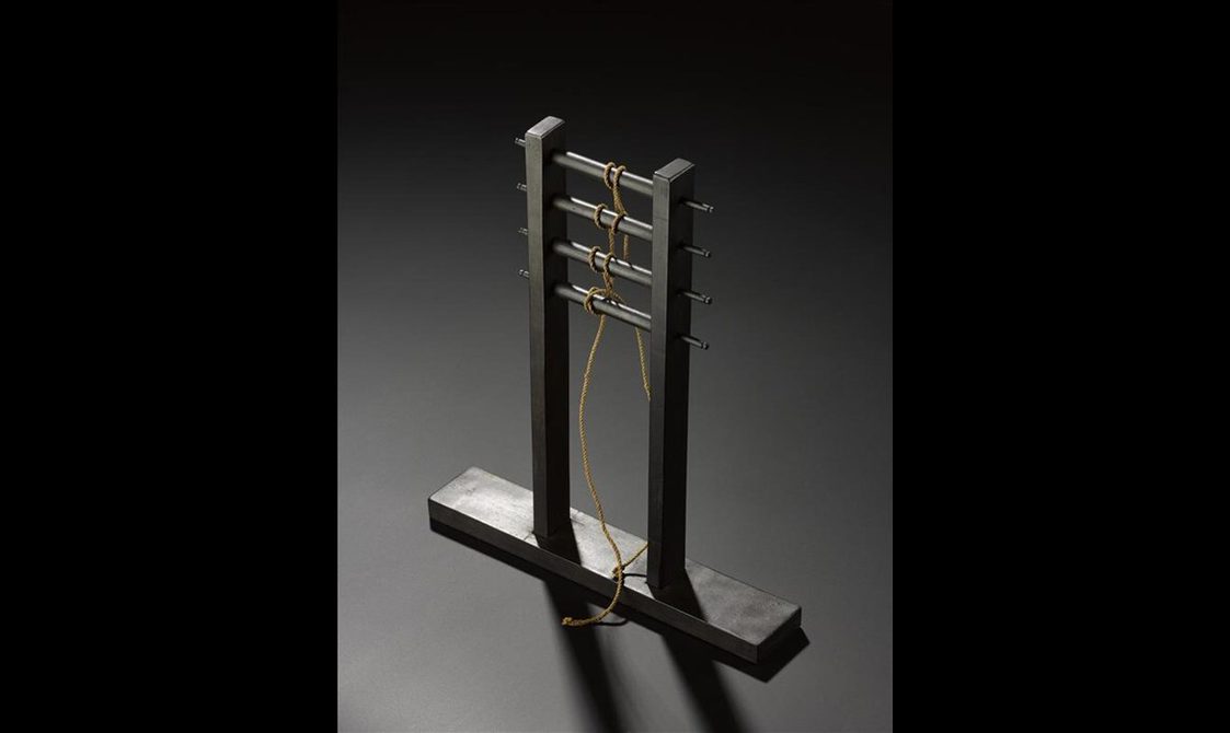 A model of a tool for making rope. It consists of two posts sitting on a rectangle with four rungs between the posts.