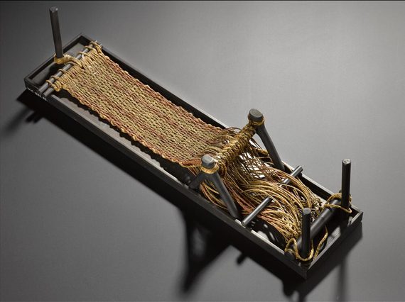 A small rectangular loom with yellow and orange fibres being woven into a textile.
