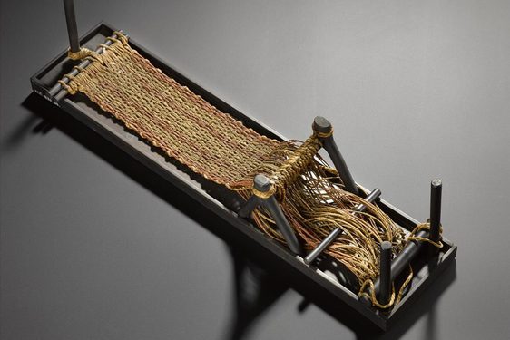 A small rectangular loom with yellow and orange fibres being woven into a textile.