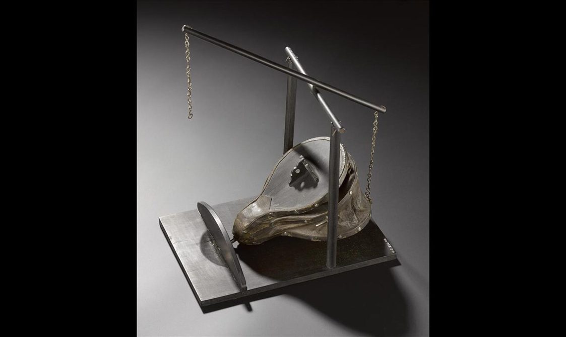 Model of a blacksmith's bellows sitting within a frame on a rectangular piece of wood