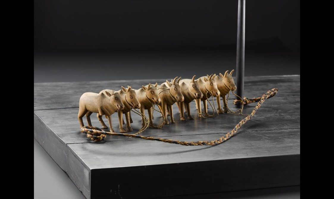 Models of seven oxen standing in a row with rope attaching them to a wooden pole.