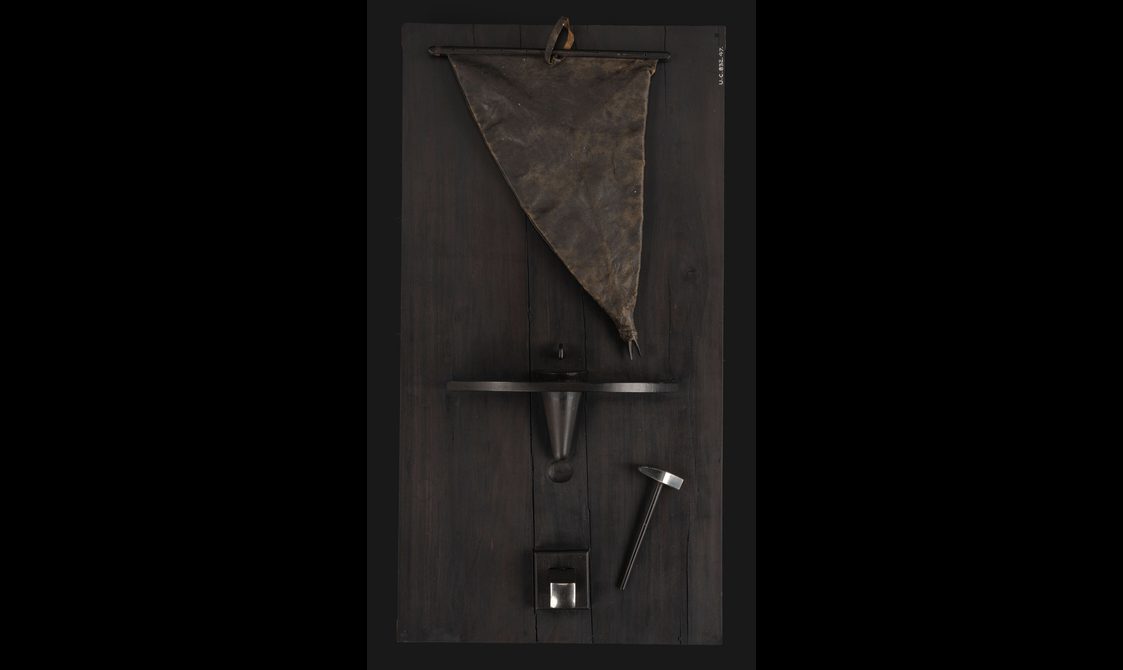 A dark wood panel with a small hammer and other tools for a blacksmith
