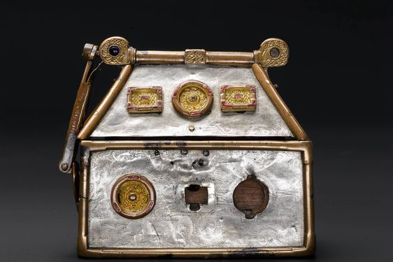 A small silver box with gold metal work along the edges. There are gold mounts of different shapes embedded on the box.