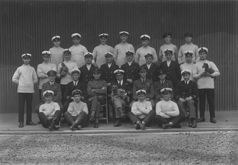 A black and white photograph of a navy crew arranged in 3 rows in both formal and casual dress.