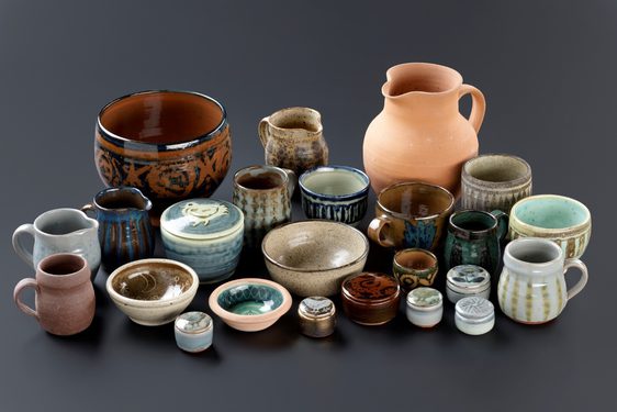 A large group of pots, mugs, jugs, and bowls in different styles on a grey background.