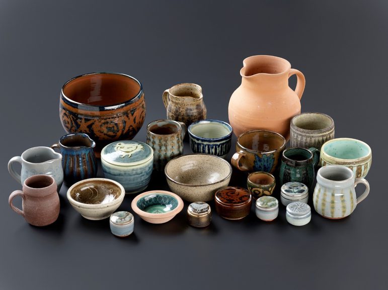 A large group of pots, mugs, jugs, and bowls in different styles on a grey background.