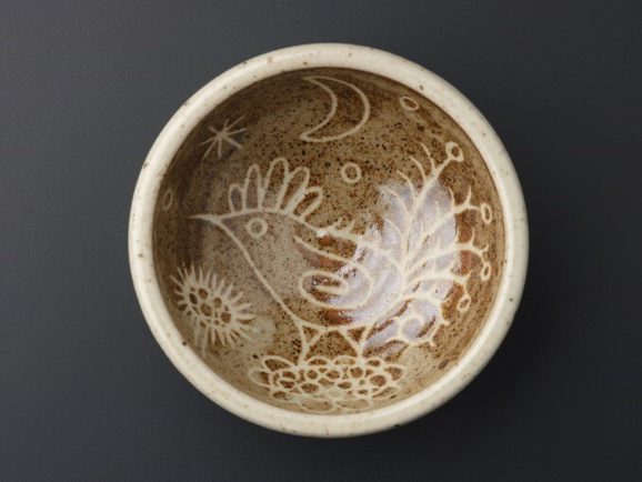 A bowl viewed from above. It has a white rim and a white bird pattern on brown glazed background inside.