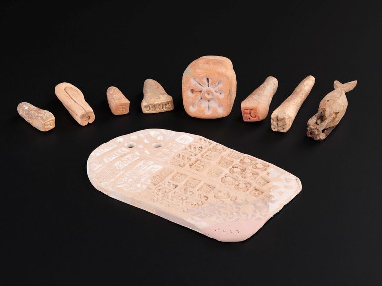 Different sizes and shapes of stamps made out of unglazed clay. There is a slab in front of them showing the stamp patterns.