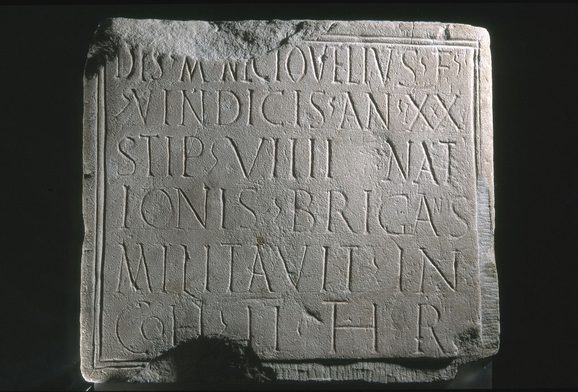 Close-up of a a grey stone slab with Latin text written in neat rows across its whole surface.