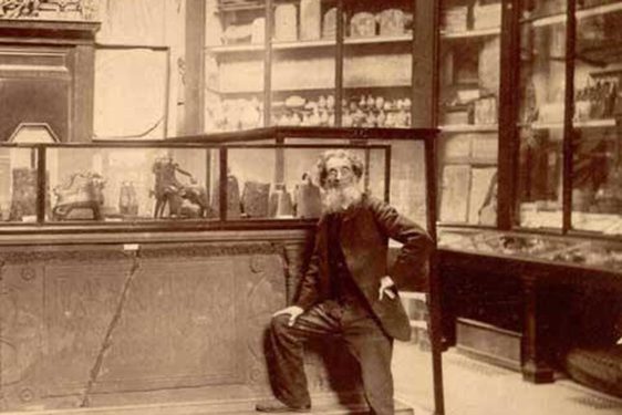 A man photographed standing with one leg raised on a plinth in front of museum case displays. Large display cabinets are visible in the background.