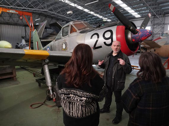 Two visitors listening to a man talking in front of an aircraft.