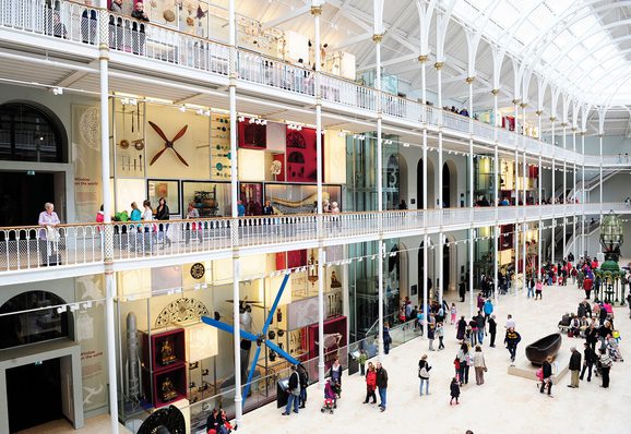 A multi-level open museum space with balconies and an arched ceiling. There are lots of visitors looking at objects on display.