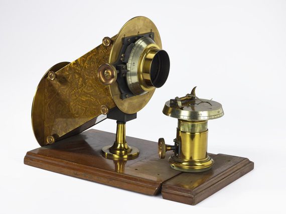 A brass metal tool mounted on a wooden base with a small elevated dial and a tube aimed at the dial.