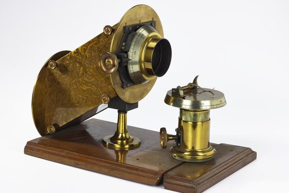 A brass metal tool mounted on a wooden base with a small elevated dial and a tube aimed at the dial.