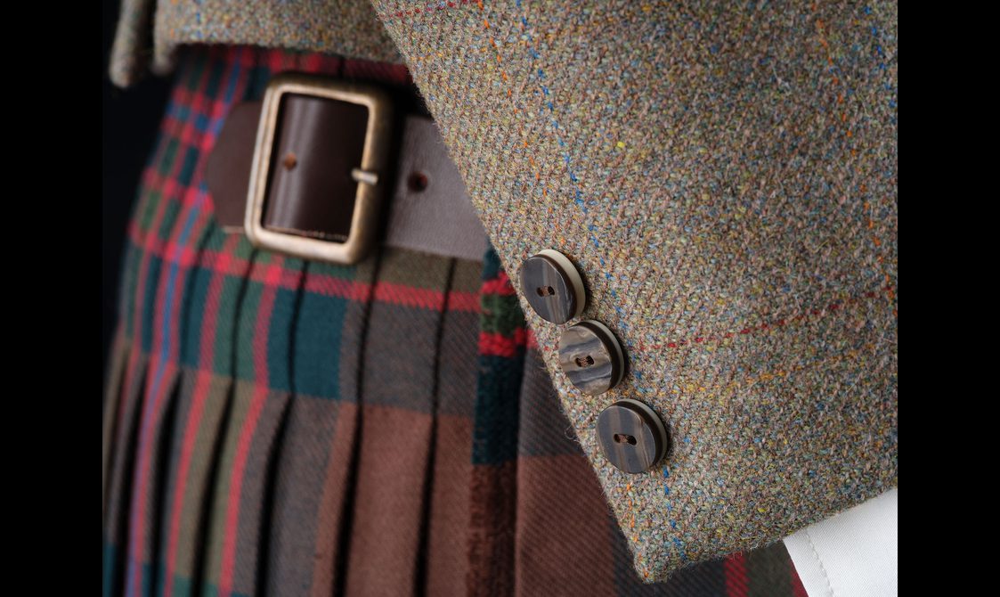 A close up of a mannequin wearing a red, blue, and green tartan kilt and a light brown tweed jacket.