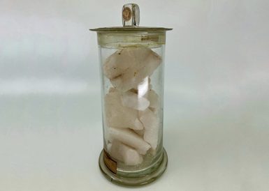 A glass jar with blocks of pale pink nitre.