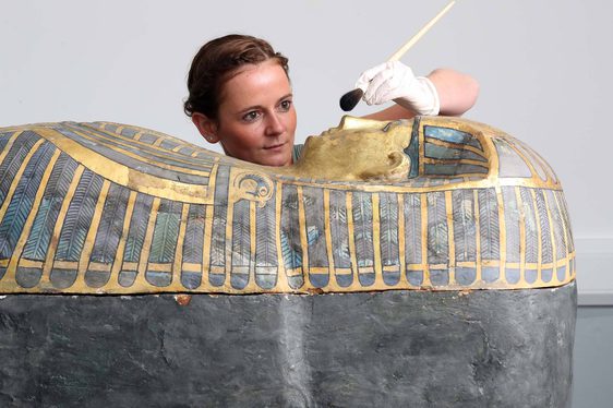A conservator cleaning the top of a sarcophagus with a brush.