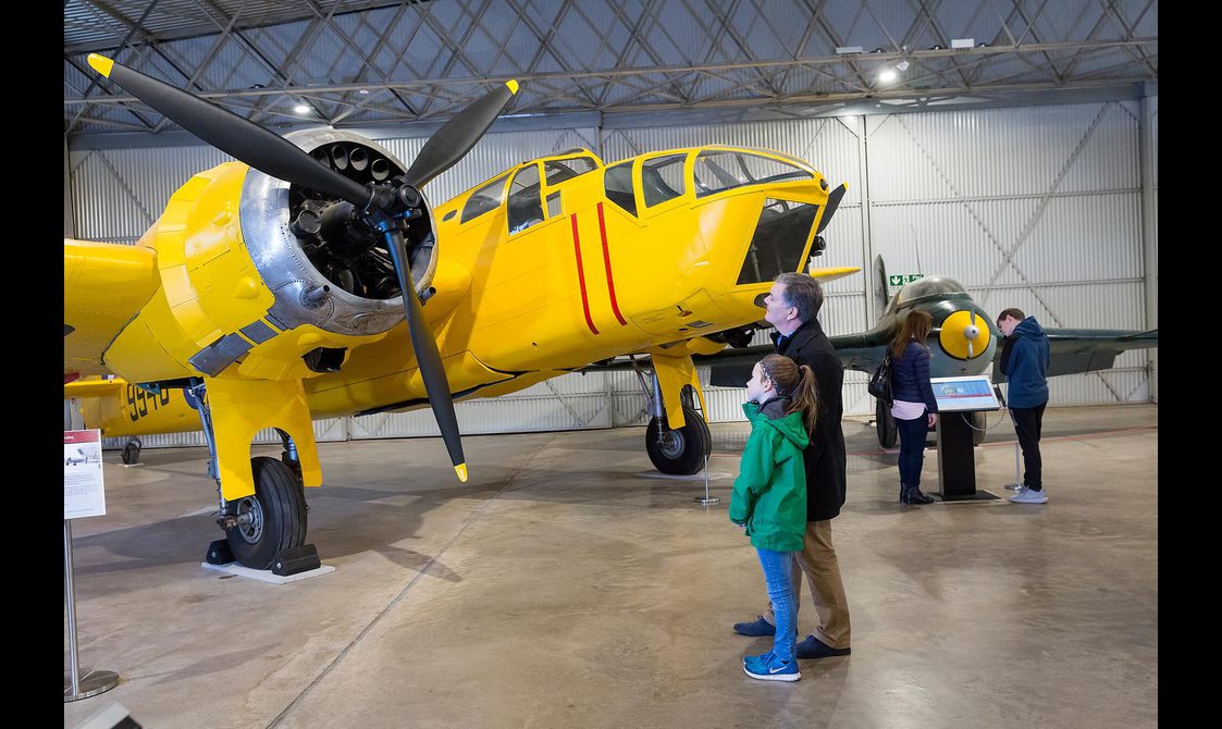 Visitors looking at a yellow Bristol Bolingbroke aircraft in the Military Aviation hangar.