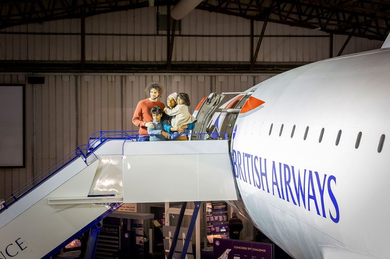 A family of four standing on boarding steps outside the door of a Concorde aeroplane.