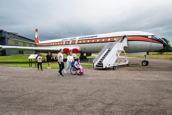 A family of five pass by a parked de Havilland Comet aircraft in an airfield.