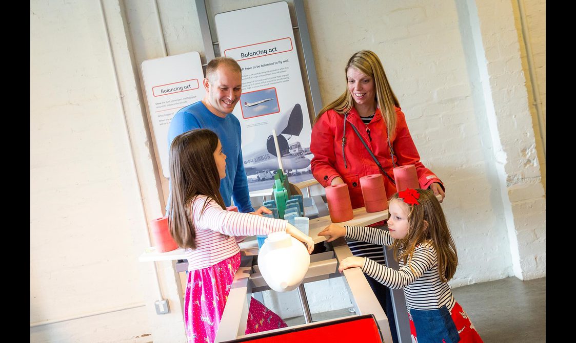 A family of four playing with a balancing game in the Fantastic Flight gallery.