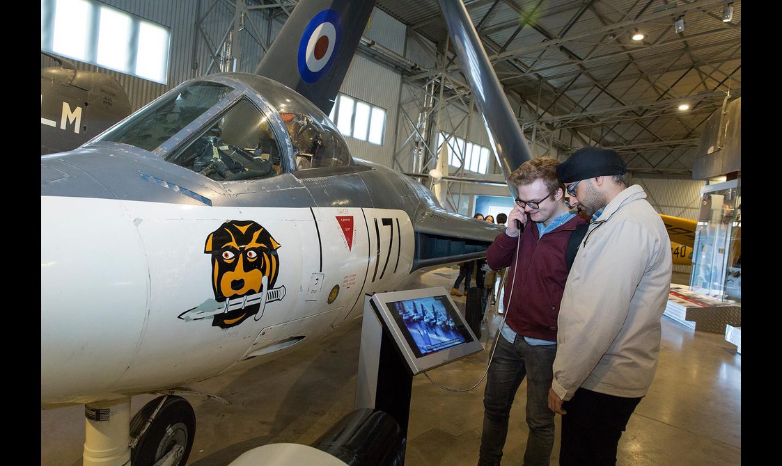 Two visitors listening to a video next to a Hawker Sea Hawk aircraft in the Military Aviation hangar.