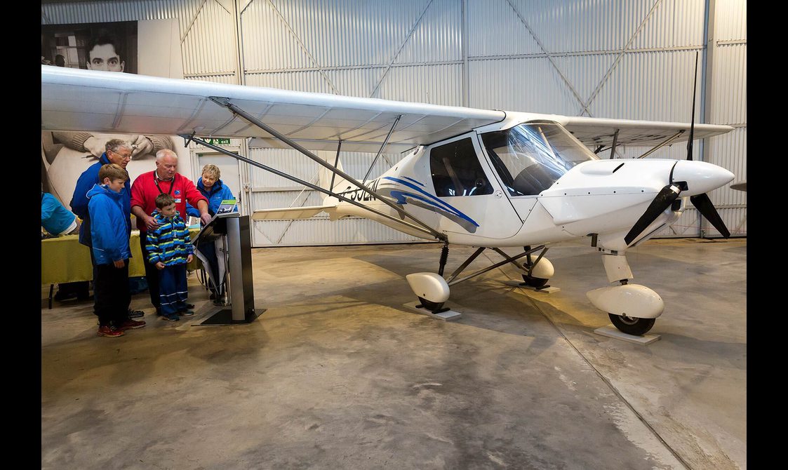 Visitors looking at a screen next to an Ikarus C42 aircraft in the Civil Aviation hangar.