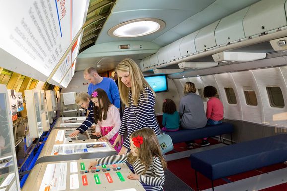 Adults and children interacting with hands-on displays in an aeroplane cabin.