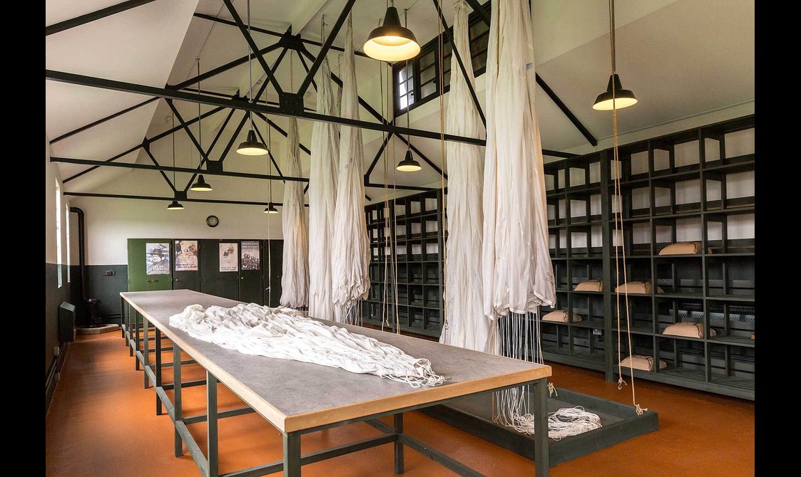 A large room with old white parachutes hanging from the ceiling and spread across a long table.