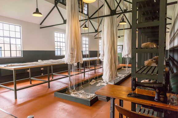 A large room with old white parachutes hanging from the ceiling and spread across a long table.