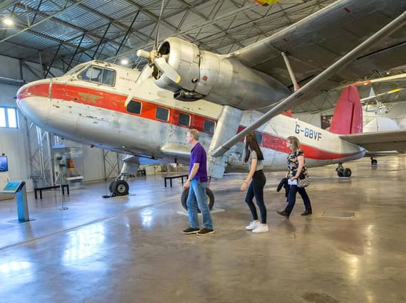 A family walking underneath the wing of a Twin Pioneer aircraft in the Civil Aviatio hangar.