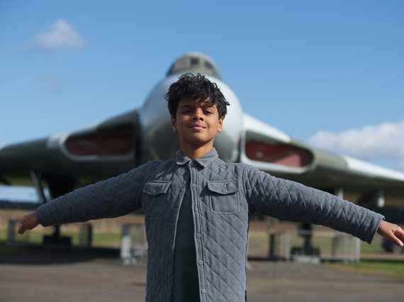 A child with their arms spread out wide, mimicing the wings of a Vulcan aircraft in the background.