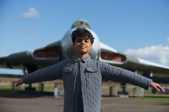 A child with their arms spread out wide, mimicing the wings of a Vulcan aircraft in the background.