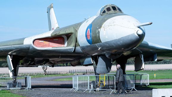 A curator walking underneath an Avro Vulcan aircraft on display in an airfield.