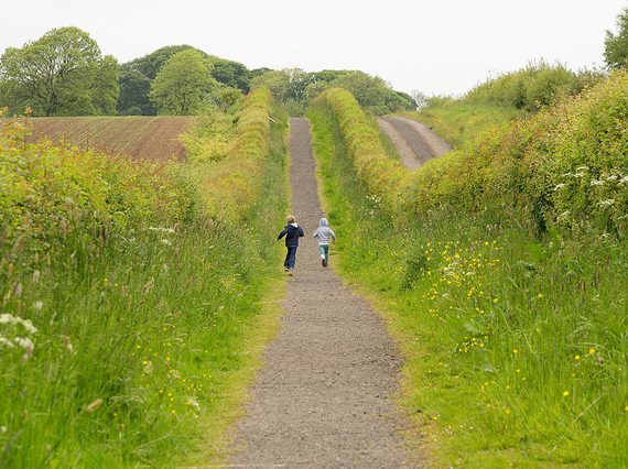 Two children run down a hedge-lined path ion the countryside.
