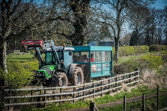 A green tractor pulling a trailor of people along a countryside road.