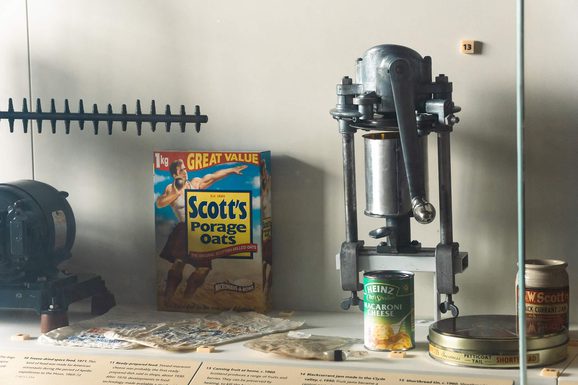 A museum display case with food packaging on the inside, including a Scott's porage oats box and a can of Heinz macaroni cheese.