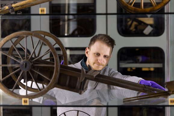 A curator looking at a small model of a wooden farming cart on a glass shelf in the study store.