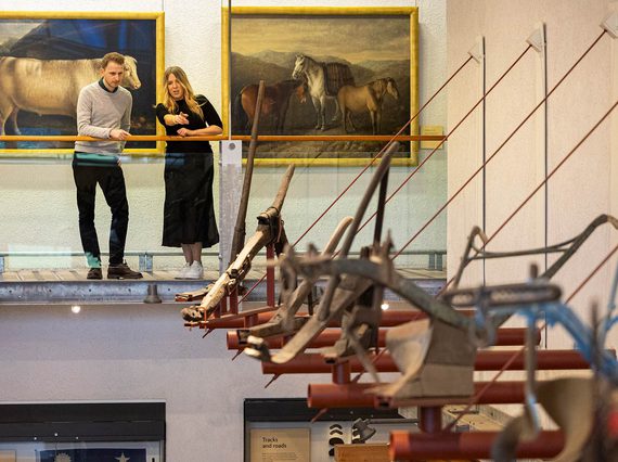 Two curators looking at a row of farming equipment hanging on the wall of the Tools gallery at the National Museum of Rural Life.