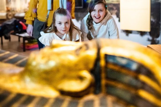 A family of three looking at the head of a sarcophagus in a museum gallery.