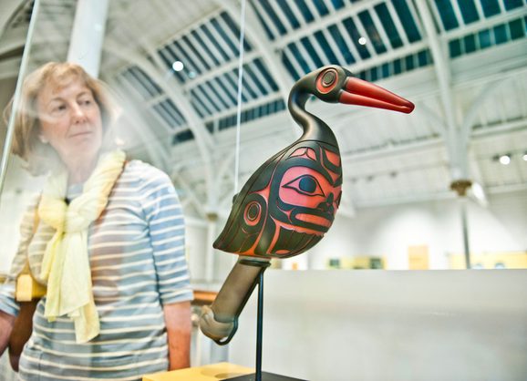 A visitor looking at sculpture of a black and red oystercatcher rattle in a glass display case.