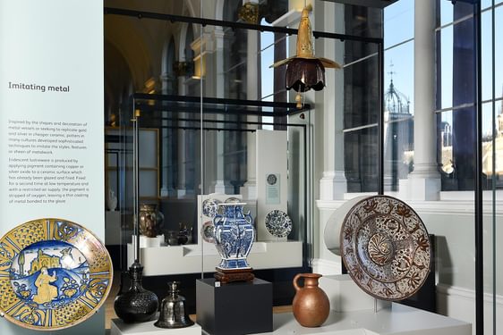 A museum case with examples of colourful ceramic plates, jugs, and vases.
