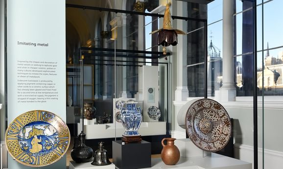 A museum case with examples of colourful ceramic plates, jugs, and vases.