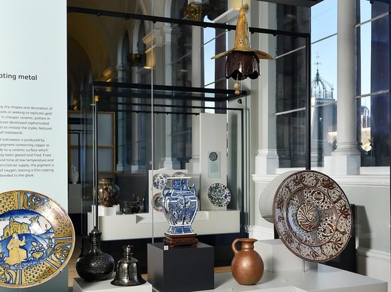 A museum case with examples of colourful ceramic plates, jugs, and vases.