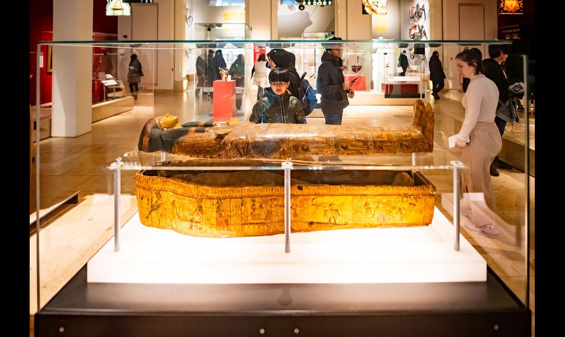A child looking at a sarcophagus in a glass case.