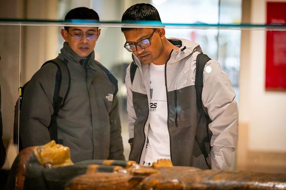 Two visitors looking at a sarcophagus in a museum display case.