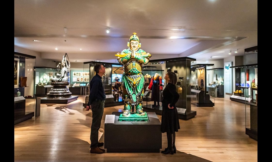 Two visitors in a museum gallery looking up at a sculpture of Weituo.