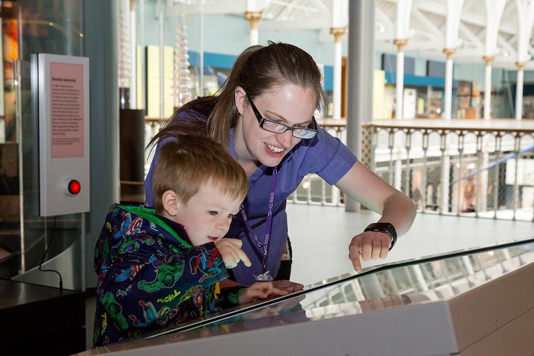 A member of staff shows a young child how to play with an interactive screen in a museum.