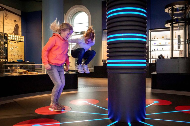 Two children jumping on coloured lights on the floor of a museum gallery.